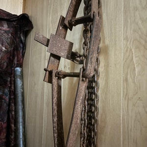 May include: A rusty metal chain hoist with multiple chains hanging from it. The hoist is attached to a wooden wall.