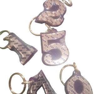 May include: Five gold-colored keychains with key rings. Each keychain features a different number, 1, 2, 5, 7, and 9, with a repeating pattern of the word "DWO" on the front.