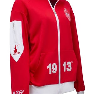 May include: Red zip-up jacket with white accents. Features a white collar, cuffs, and a white panel on the left chest with a logo and text. The number "1913" is displayed on the front.