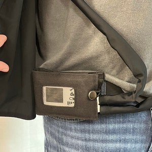 May include: A black and gray pouch with a clear window and a black button. The pouch is attached to a black belt.