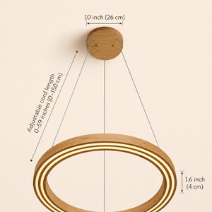 May include: Wooden ring chandelier with dimensions displayed. The light fixture is made of wood and features a circular design with a built-in light. The ring is 23 inches (58 cm) in diameter, 1.6 inches (4 cm) thick, and has an adjustable cord length of 0-59 inches (0-150 cm).