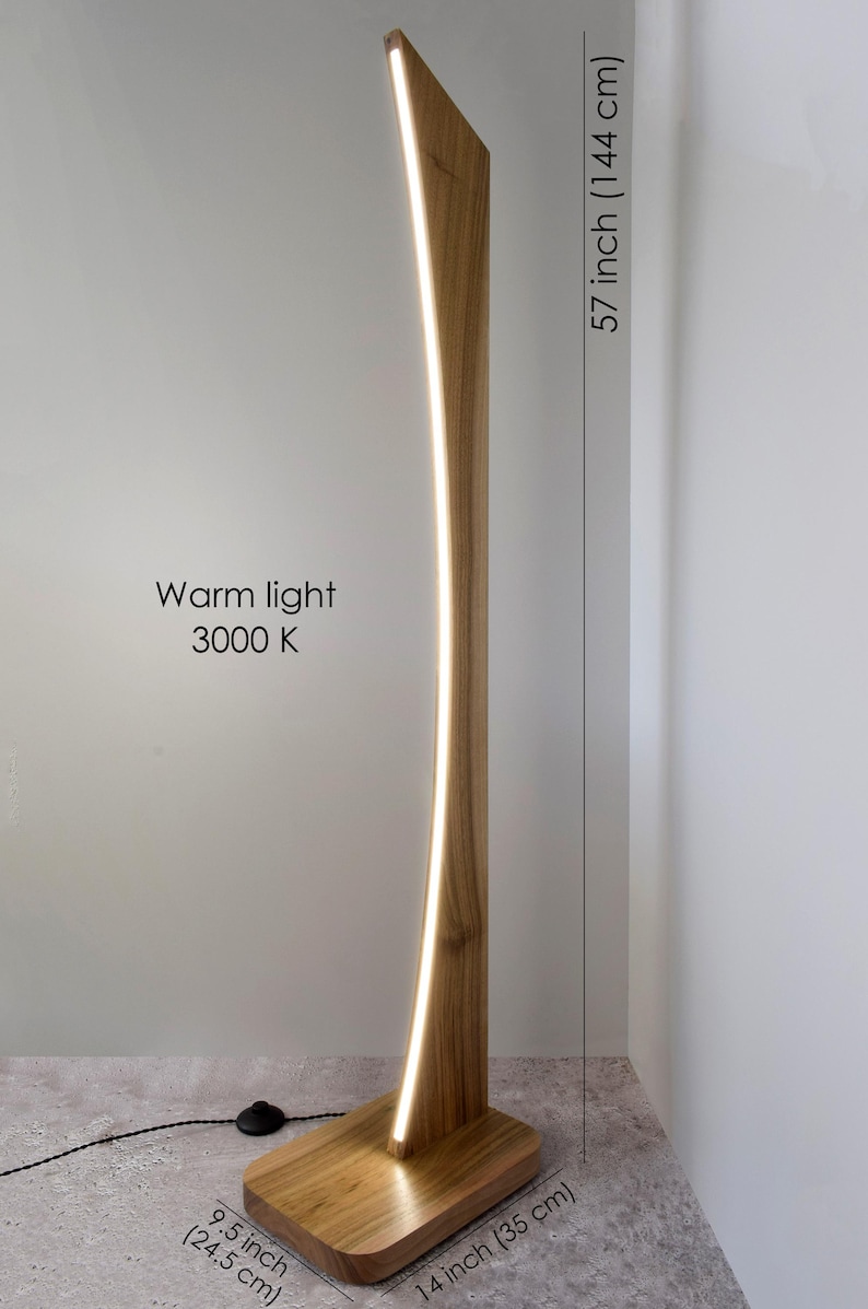 May include: A wooden floor lamp with a curved design, featuring a warm light (3000 K) that runs along its length. The lamp is 144 cm tall, with a base of 35 cm by 24.5 cm.