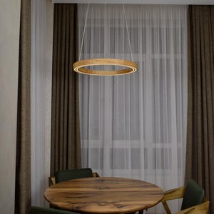May include: A modern wooden ring pendant light fixture hangs above a round wooden table and chairs. The light has a warm, inviting glow. The room has brown curtains and sheer white curtains.