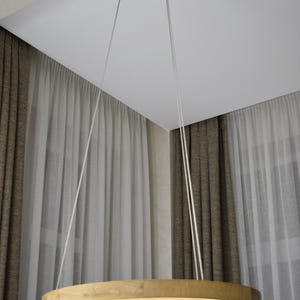 May include: A modern, circular wooden pendant light fixture. The light is suspended from the ceiling by three white cords. The light has a warm, inviting glow, and is made of light-colored wood.