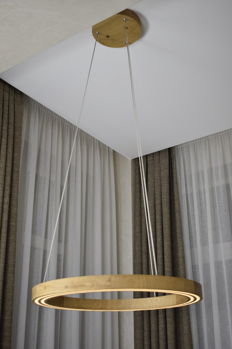 May include: A modern, circular wooden pendant light fixture. The light is suspended from the ceiling by three white cords. The light has a warm, inviting glow, and is made of light-colored wood.