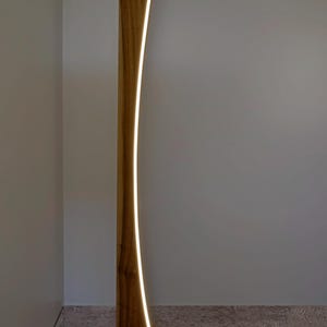 May include: A contemporary wooden floor lamp with a curved design. The lamp has a warm, natural wood finish and a bright, vertical LED light strip. The lamp is a stylish addition to any living space. The lamp's height is approximately 170 cm.