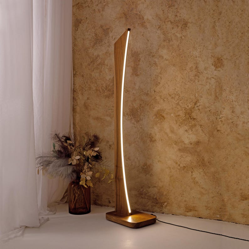 May include: A contemporary wooden floor lamp with a curved design and an integrated LED light. The lamp features a rectangular base and a tall, slender wooden frame. The light strip follows the curve, emitting a warm glow. The lamp is approximately 152 cm tall.