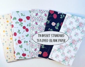 May include: Five rectangular paper inserts for a traveler's notebook, featuring various patterns including bees, cherries, floral trellis, and pink roses. The text TN INSERT STANDARD TEA DYED BLANK PAPER is printed in the center.