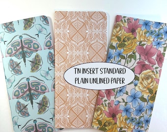 May include: Three rectangular notebook inserts with plain unlined paper. The left cover is light blue with pink and green moths. The center cover is tan with a white geometric pattern. The right cover features yellow and pink flowers. Text reads: TN INSERT STANDARD PLAIN UNLINED PAPER.