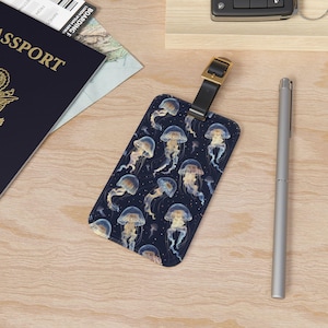 May include: A dark blue luggage tag with a repeating pattern of jellyfish in shades of blue, yellow, and white. The tag has a black leather strap and a gold metal buckle.