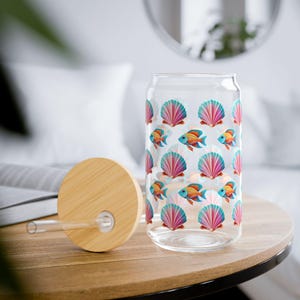 May include: A clear glass reusable water bottle with a bamboo lid and straw. The bottle has a colorful pattern of pink seashells and orange fish.