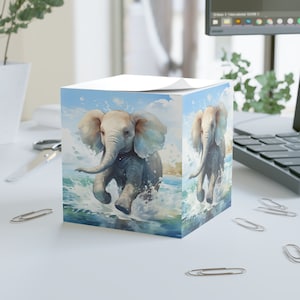 May include: A white notepad with a blue and white illustration of a baby elephant running through the water. The elephant has large ears and a trunk that is raised in the air. The water is splashing around the elephant.