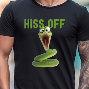 Könnte beinhalten: Ein schwarzes Kurzarm-T-Shirt mit einer Grafik einer grünen Cartoon-Schlange mit weit aufgerissenen Augen und offenem Maul. Über der Schlange ist der Text HISS OFF in grünen Großbuchstaben mittig auf der Vorderseite des T-Shirts aufgedruckt.