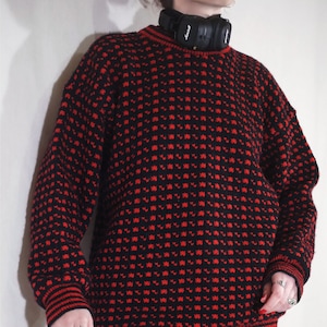 May include: A black and red knitted sweater with a geometric pattern. The sweater has a crew neck and long sleeves.