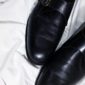 May include: A pair of black leather shoes with a buckle strap. The shoes have a polished finish and a classic design.