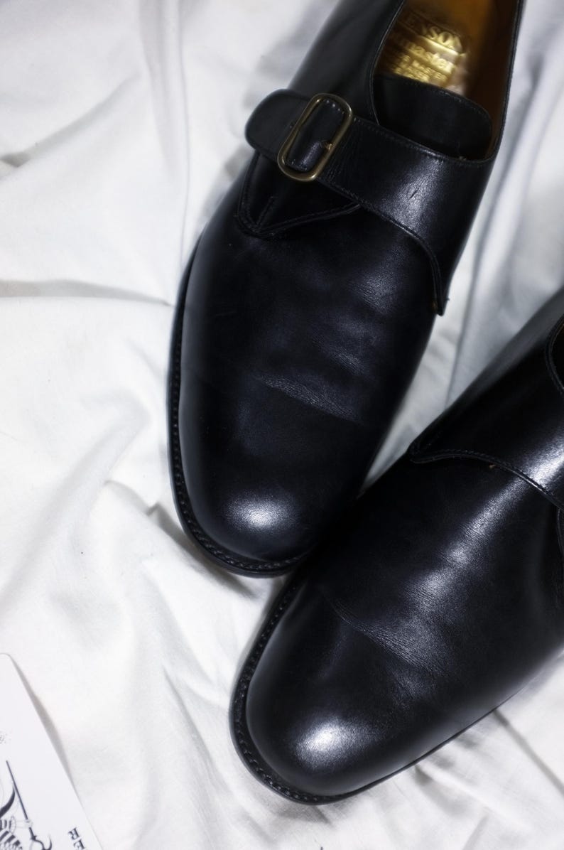 May include: A pair of black leather shoes with a buckle strap. The shoes have a polished finish and a classic design.