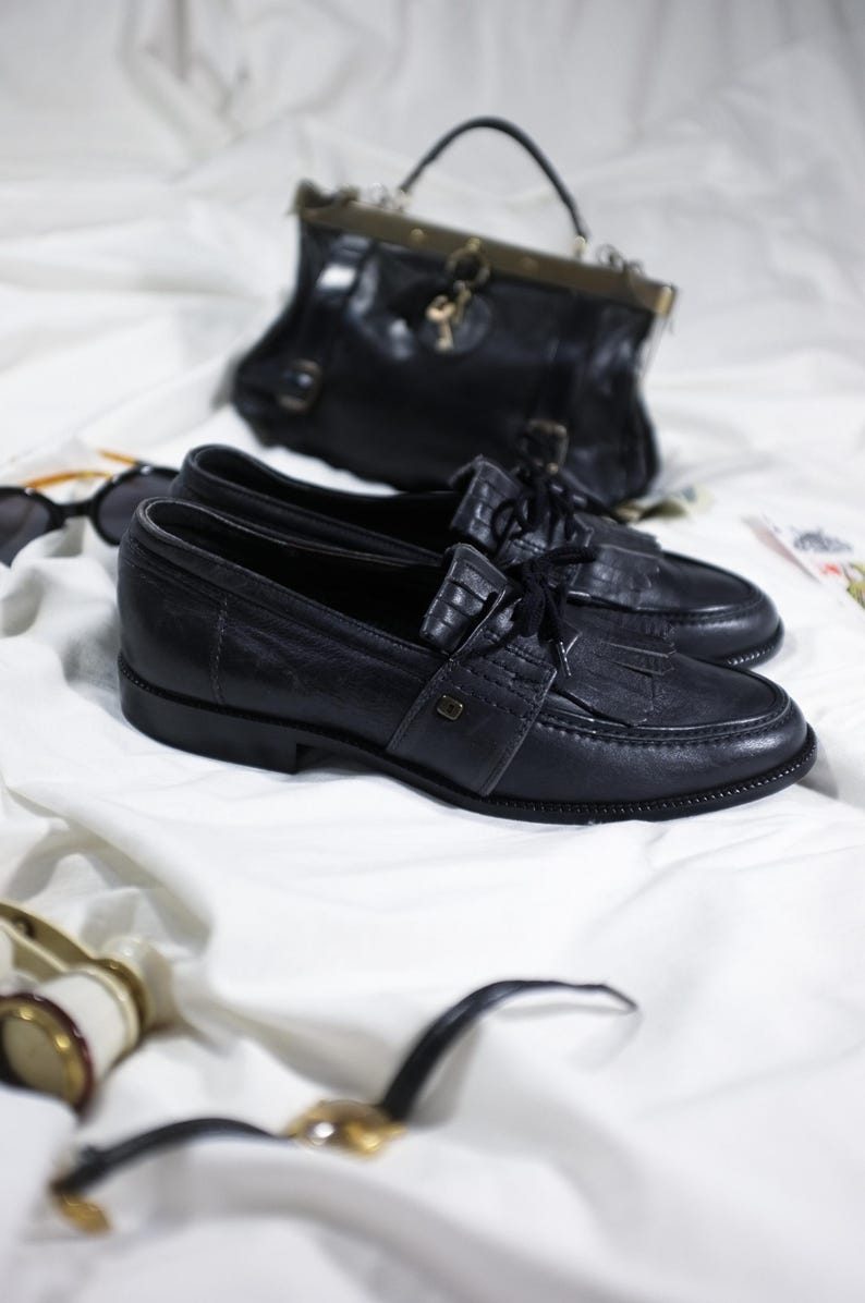 May include: A pair of black leather loafers with a tassel detail and laces. The shoes are on a white surface.