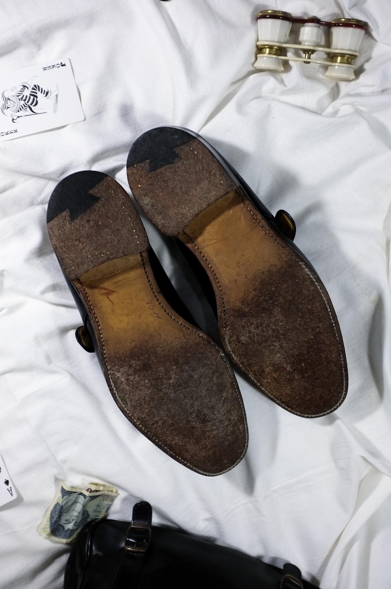 May include: A pair of black leather shoes with a brown leather sole. The shoes have a buckle strap and a pointed toe.