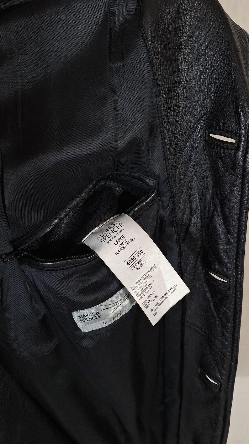 May include: Black leather jacket with a visible interior pocket and a tag from Marks & Spencer. The jacket has a classic design with visible stitching and button details. The tag indicates the jacket is a size Large.