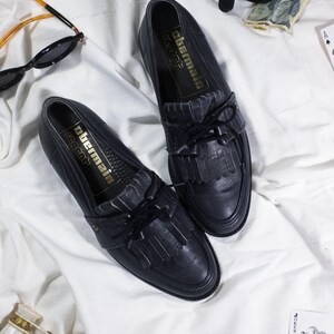 May include: A pair of black leather tassel loafers with a gold label that reads "Obermain Regent".
