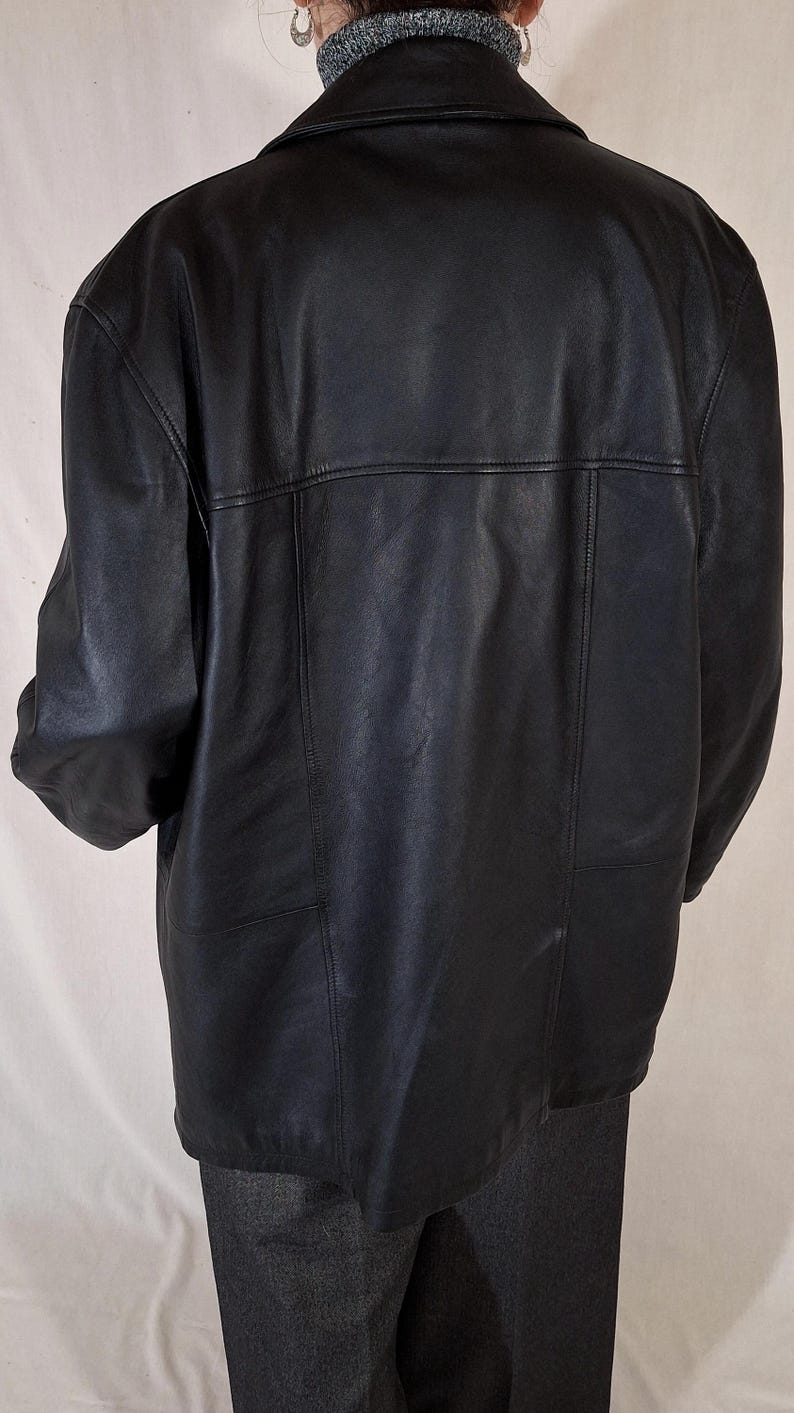 May include: Black leather jacket with a collared neckline and a tailored fit. The jacket features a classic design with a smooth, matte finish. The back of the jacket has a horizontal seam across the upper back and vertical seams.