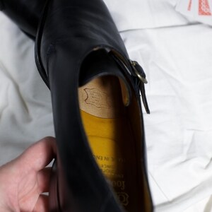 May include: Black leather dress shoe with a buckle closure. The shoe has a yellow leather insole with the text "Goodrich" and "Established Since 1902" printed on it. The text "Made in England" is also printed on the insole.