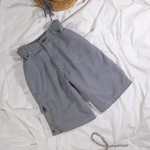 Könnte beinhalten: Schwarz-weiß karierte Shorts mit einer Tasche auf der linken Seite, ein Strohhut, eine silberne Kettenkette und schwarze Kopfhörer auf weißem Hintergrund.