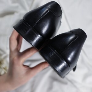 May include: A pair of black leather dress shoes with a polished finish. The shoes are shown from the bottom, showcasing the soles.