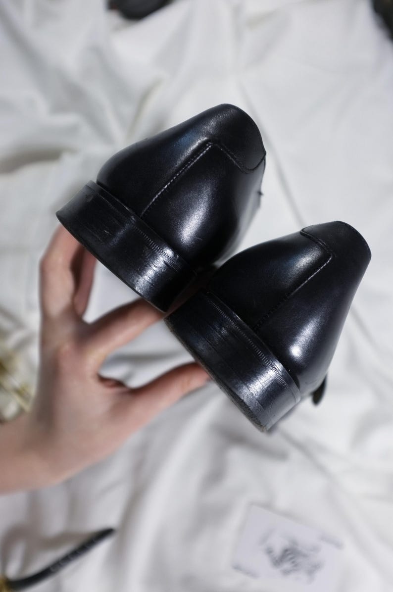 May include: A pair of black leather dress shoes with a polished finish. The shoes are shown from the bottom, showcasing the soles.