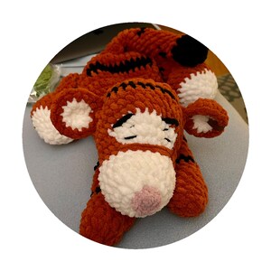 Puede incluir: Un juguete de peluche de tigre naranja y negro hecho a mano. El tigre tiene detalles blancos en la cara, las orejas y las patas, con una nariz rosa y rayas negras. El juguete est&aacute; hecho de hilo suave y texturizado.