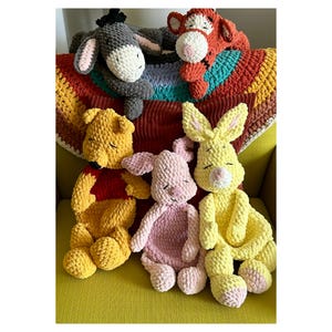 Puede incluir: Colecci&oacute;n de peluches hechos a mano con personajes de un popular libro infantil. Los juguetes incluyen un oso amarillo, un cerdo rosa, un conejo amarillo, un burro gris y un tigre naranja. Est&aacute;n colocados sobre una manta colorida.