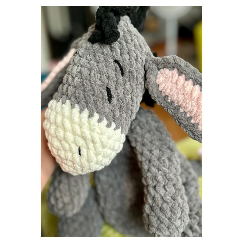 Puede incluir: Un juguete de peluche de burro gris y blanco hecho a mano con ojos negros y una melena negra. Las orejas del burro tienen detalles internos rosas. El juguete est&aacute; hecho de un material suave y texturizado.