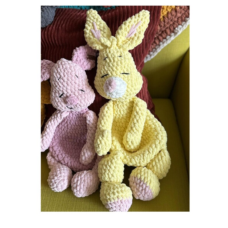 Puede incluir: Dos animales de peluche hechos a mano con ganchillo: un conejo amarillo y un cerdo rosa. El conejo tiene orejas largas con detalles rosas, una nariz blanca y ojos cerrados. El cerdo tiene orejas ca&iacute;das y ojos cerrados. Ambos est&aacute;n hechos de hilo suave y texturizado.