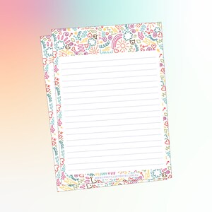 May include: A set of two white lined notepads with a colorful doodle border featuring hearts, stars, clouds, rainbows, and lightning bolts. The border includes the text "www.cakevillustrat.com.au".