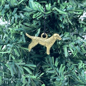 May include: Gold-colored metal ornament shaped like a dog hanging on a green artificial Christmas tree.