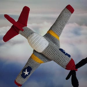 May include: A crocheted airplane toy with gray, red, white, and yellow details. The airplane has a propeller and a star on the wing.