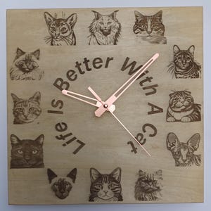 Könnte beinhalten: Quadratische Holzuhr mit hellem Holzfinish, mit eingravierten Katzenporträts am Rand. Die Uhrzeiger sind roségoldfarben, und der Text "Life is Better With A Cat" ist auf dem Zifferblatt eingraviert.