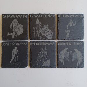 May include: Six black slate coasters with white engraved images and text. The coasters feature characters from the comic book series Spawn, Ghost Rider, Hades, John Constantine, Hellboy, and Lucifer Morningstar.