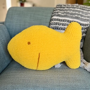 May include: A yellow crocheted fish-shaped pillow. The pillow is made of a soft, fuzzy yarn and has a simple, embroidered face.