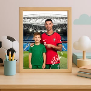 May include: A framed photo of a man and a boy wearing soccer jerseys. The man is wearing a red jersey with the number 7 and the Portuguese flag on the chest. The boy is wearing a green jersey. The man is signing his name in white ink on the photo. The background is a blurry image of a soccer stadium.