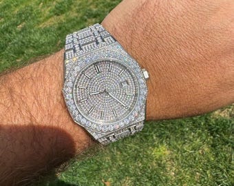May include: A silver watch with a diamond-encrusted face and band. The watch is on a person's wrist.