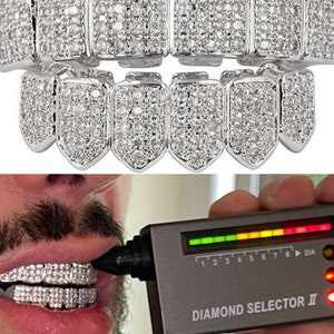 May include: A set of silver grillz with a row of small, clear stones. The grillz are being tested with a diamond selector tool, which shows a green light on the scale.
