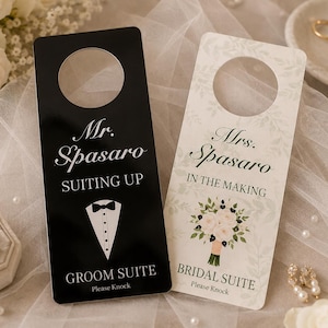 May include: Two rectangular door hangers with circular cutouts at the top. The black hanger features white text reading Mr. Spasaro SUITING UP GROOM SUITE Please Knock and a tuxedo graphic. The white hanger features floral accents and text reading Mrs. Spasaro IN THE MAKING BRIDAL SUITE Please Knock.