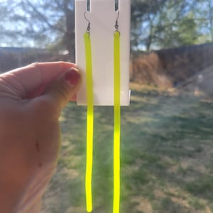 May include: A pair of long, bright yellow dangle earrings. The earrings are made of a thin, flexible material and hang from silver hooks.