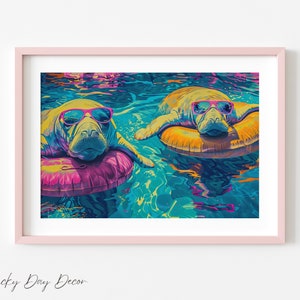 Op de afbeelding: Een ingelijste kunstdruk met twee zeekoeien met zonnebrillen, drijvend in turquoise water op opblaasbare ringen. De zeekoeien zijn geel en blauw, en de ringen zijn roze en oranje. De print zit in een roze lijst.