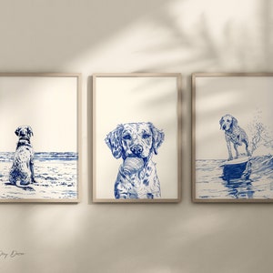 以下が含まれることがあります： ビーチで犬を描いた額装されたイラストが3つあります。最初のイラストは、犬がビーチに座って海を見つめている様子です。2番目のイラストは、犬がボールをくわえている様子です。3番目のイラストは、犬が波に乗っている様子です。