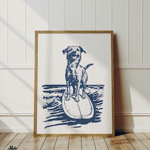 May include: A framed print featuring a navy blue illustration of a dog surfing. The dog is standing on a surfboard in the ocean, with a happy expression. The print is in a wooden frame and is displayed against a white wall.