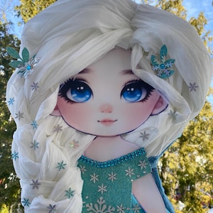 May include: A blue and white pinata shaped like a girl with long white hair and a blue dress. The pinata has a sparkly blue and silver snowflake design on the dress.