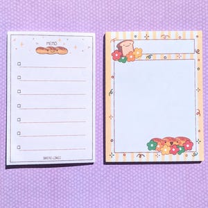 Può includere: Due blocchi note a tema pane. Il blocco note a sinistra ha uno sfondo bianco con un'illustrazione di pane marrone e il testo "MEMO" e "BREAD LINGS". Il blocco note a destra ha uno sfondo a strisce giallo e bianco con un'illustrazione di pane marrone e fiori.