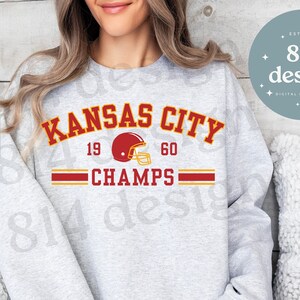 May include: Gray sweatshirt with the text "KANSAS CITY" in red and black lettering, a red football helmet graphic, and the text "19 60 CHAMPS" in red and black lettering.